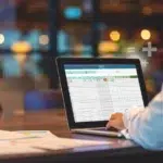An accountant workspace with an accounts payable spreadsheet displayed on a laptop next to a calculator and invoices