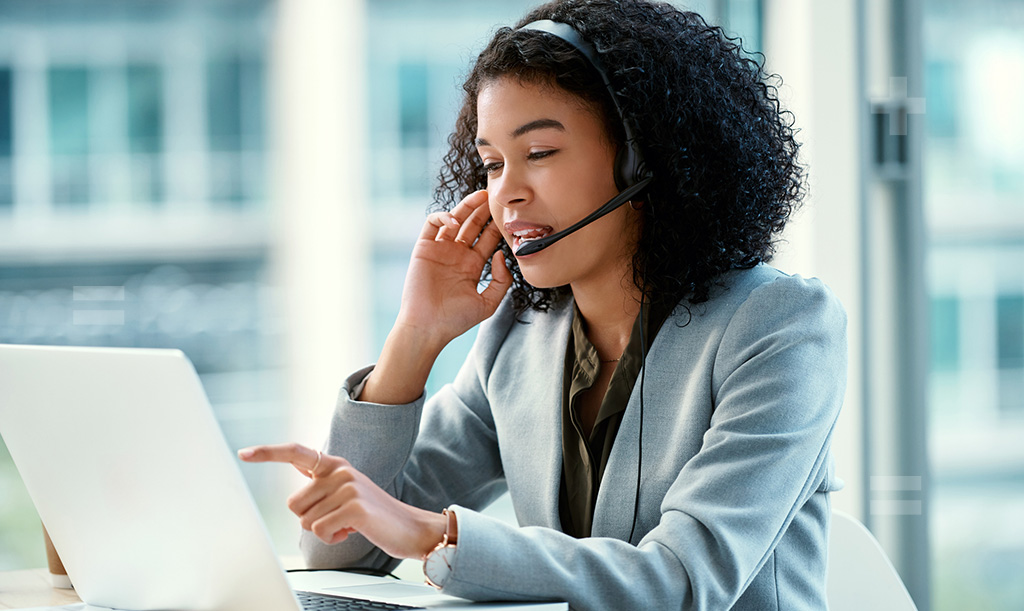 A female working professional working on a laptop while wearing a headset.