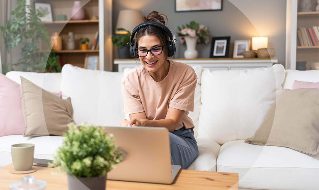 A woman seated on a couch wearing a headset and talking to someone through her laptop