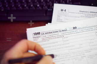 A person calculating their federal income tax bill using IRS Form 1040 and a calculator