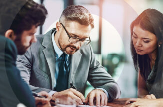 An accounting executive signing documents for two executive assistants seated at a desk.